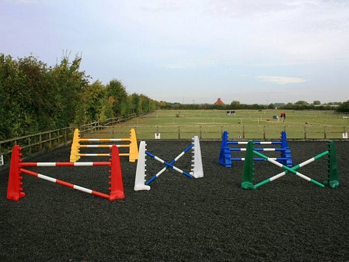 From left to right, 1 pair of red 8 cups with 2 5 band poles in red and white. 1 pair of yellow 8 Cups and yellow MultiJumps with 3 5 Band Poles. In the centre is a pair of white 8 Cups with 2 5 Band Pole in blue and white. 1 pair of blue 8 Cups and Blue MultiJumps with 3 5 Band Poles in blue and white. On the right is a pair of green 8 Cups with 2 green and white poles. All jumps in an arena.