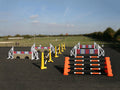 Photograph of the PolyJumps Advanced set in an arena. The set's contents are as follows: 1 set of Combi Blocks, 4 sets of Cross Wings and 3 sets of 8 Cups with 4 Bridge Fillers and 21 Poles. This set's colour scheme is varied, from Orange to Yellow to White.