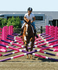Photograph of horse and rider jumping over the PolyJumps Carol Mailer Grid Set, comprised of 14 Pink 8 Cups and 14 9 Band Pro Poles coloured: Purple, White & Pink. 
