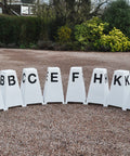 8 Dressage Tower Markers sat on gravel. Black painted letters on all sides (A, B, C, E, F, H, K, M).