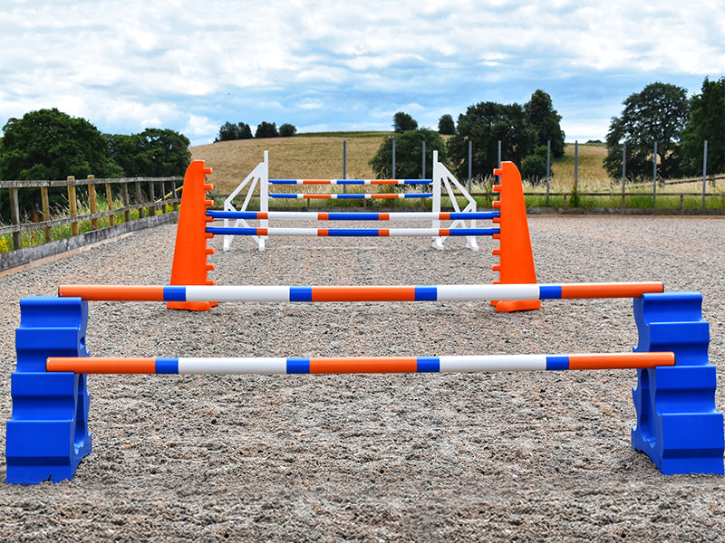 Blue MultiJumps with 9 Band Poles coloured Orange, Blue and White. Behind that, 2 orange 8 Cups with 9 band poles coloured: Blue, Orange and white. At the back White Cross wings with 9 band poles coloured Blue, white and orange. All jumps in arena.